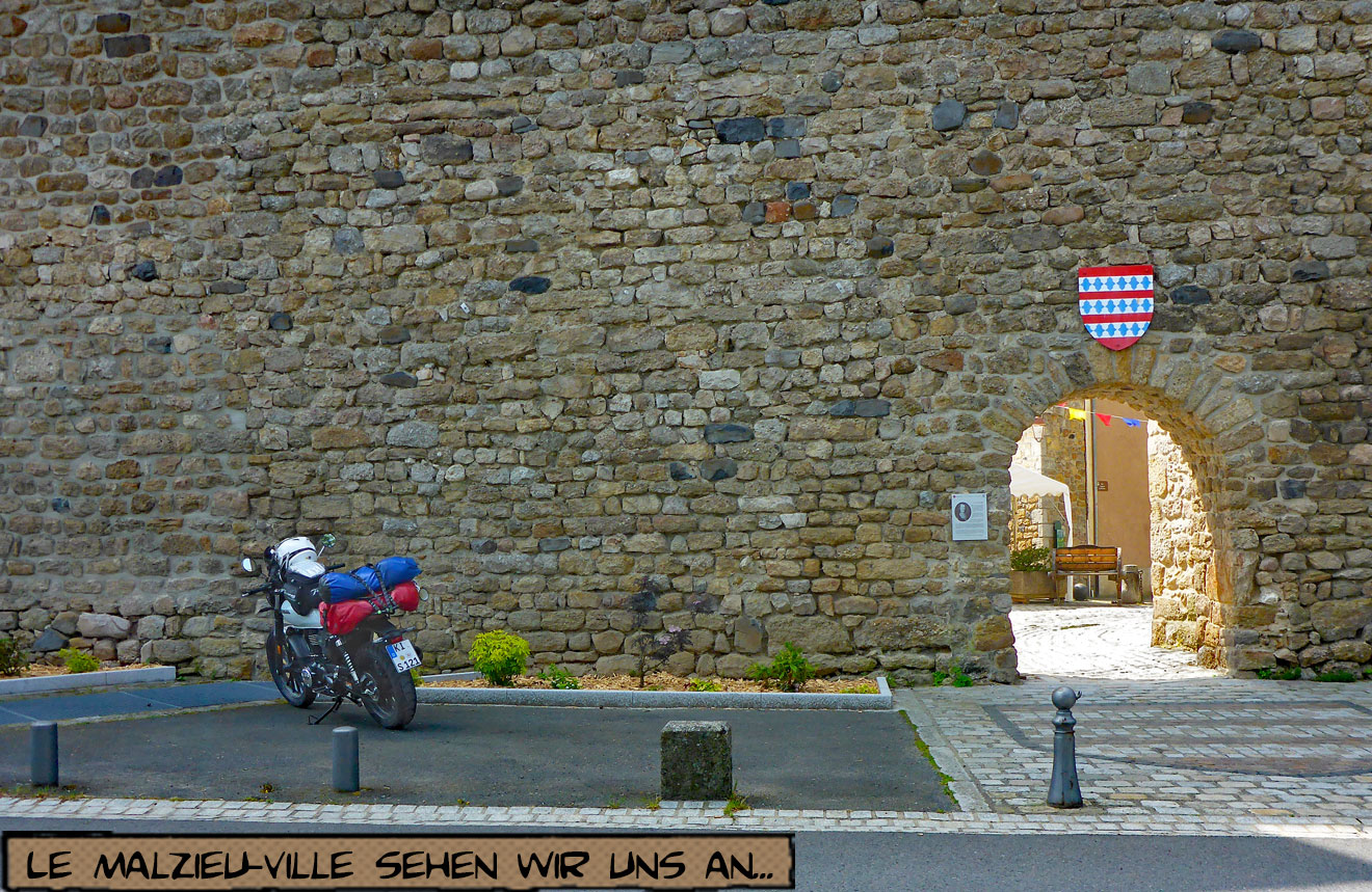Ein Motorrad steht mit Reisegepäck vor der Stadtmauer von Le-Malzieu-Ville